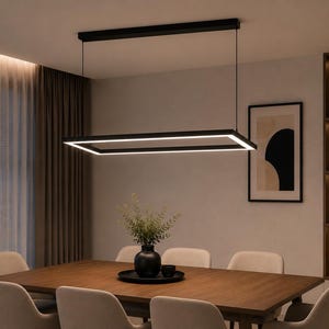Könnte beinhalten: Eine rechteckige schwarze Pendelleuchte, die mit zwei dünnen Drähten an der Decke befestigt ist. Der Rahmen verfügt über ein durchgehendes integriertes LED-Lichtband an der Innenkante, das ein helles weißes Licht auf den Holztisch wirft.