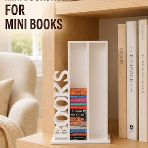 May include: A white vertical bookshelf with the word BOOKS cut out in large letters on the left side. The shelf contains a stack of miniature books with colorful spines. The text MINI BOOKSHELF FOR MINI BOOKS is visible at the top left.