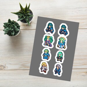May include: A sheet of eight pixel art character stickers. The stickers feature various characters in different poses and outfits, with a variety of colours including blue, green, and gold. The stickers are on a grey background.
