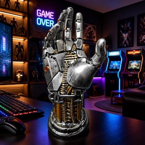 May include: A robotic hand sculpture featuring a weathered silver finish with exposed gold-colored mechanical wiring and joints. The upright hand is mounted on a circular base, showcasing intricate segmented plating and small orange circular accents.