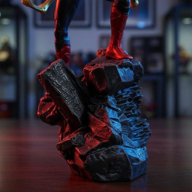 May include: A detailed figurine base featuring a dark, jagged rock formation with sharp edges and a rough, textured surface. The base supports the lower legs of a character, showing red and black suit details with blue and red ambient lighting.
