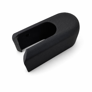 Peut inclure: Composant en plastique noir de forme rectangulaire avec un dessus incurvé et une section évidée. L'objet présente une surface texturée sur le dessus et une finition lisse. Un petit trou est visible sur le côté.