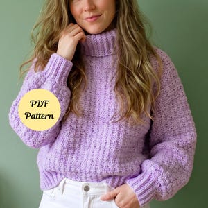 May include: A lavender long-sleeve sweater featuring a ribbed turtleneck, ribbed cuffs, and a textured knit pattern. A circular yellow graphic overlay on the left side displays the black text PDF Pattern. The sweater is paired with white denim jeans.