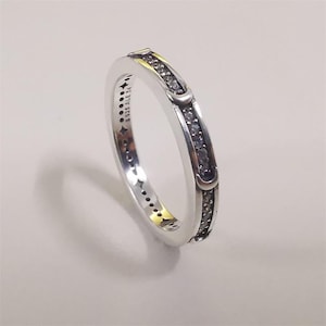 May include: A silver band ring featuring a channel of small clear stones and crescent moon accents along the outer edge. The inner band is engraved with the text S925 ALE 54 and features a series of small star-shaped cutouts along the side.
