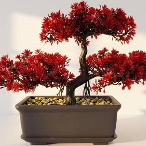 Op de afbeelding: Een kunstmatige bonsaiboom met levendig rood blad en een donkerbruine, getextureerde stam met zichtbare wortels. De boom is geplant in een rechthoekige, donkerbruine keramische pot gevuld met kleine, lichtgekleurde decoratieve steentjes.