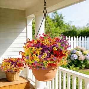 K&ouml;nnte beinhalten: Ein h&auml;ngender terrakottafarbener Pflanzk&uuml;bel gef&uuml;llt mit einem dichten Arrangement aus leuchtend bunten Blumen in Gelb-, Orange-, Rot- und Violettt&ouml;nen, aufgeh&auml;ngt an einer dunklen Metallkette an einer Veranda, mit einem passenden Korb daneben.