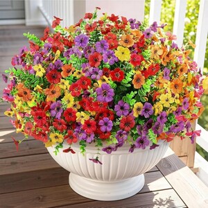 K&ouml;nnte beinhalten: Ein gro&szlig;es, rundes Arrangement aus k&uuml;nstlichen Blumen in leuchtenden Rot-, Orange-, Gelb- und Violettt&ouml;nen mit kleinen f&uuml;nfbl&auml;ttrigen Bl&uuml;ten und gr&uuml;nem Blattwerk, pr&auml;sentiert in einer wei&szlig;en, geriffelten Schale auf einem Fu&szlig;.