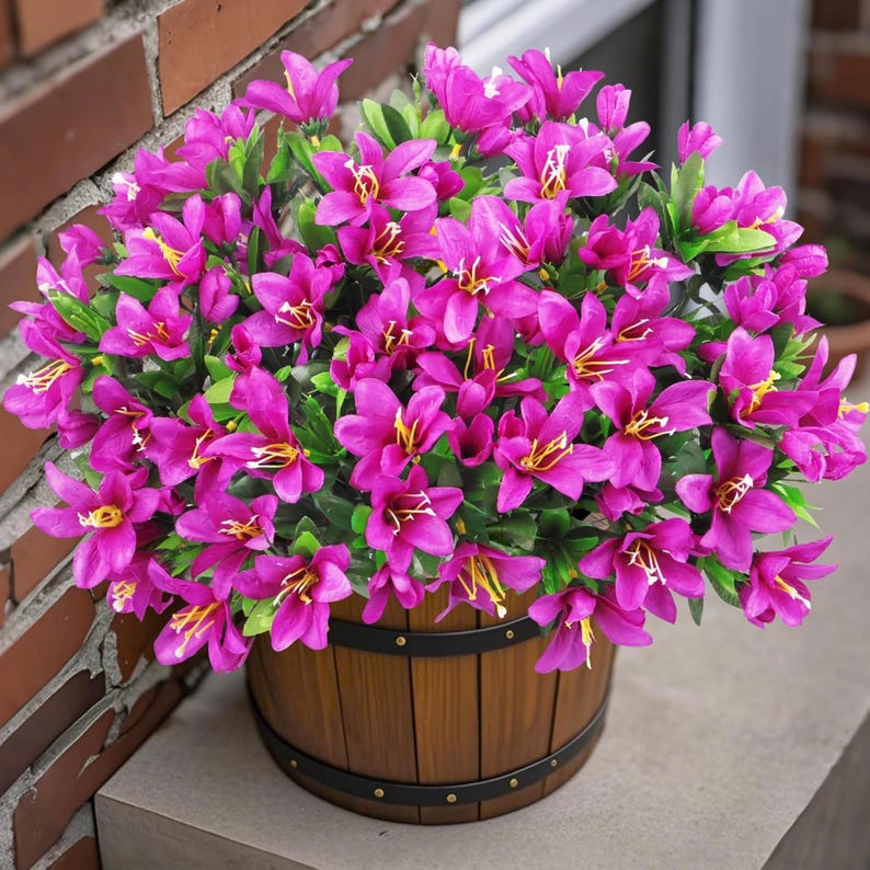 May include: A dense arrangement of vibrant magenta flowers with yellow centers and green leaves, housed in a round, brown wooden barrel-style planter featuring two horizontal black metal bands with small rivets around the exterior surface.
