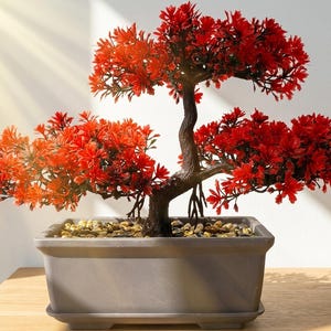 Op de afbeelding: Een decoratieve kunstmatige bonsaiboom met levendig rood blad en een donkerbruine, getextureerde stam. De boom is geplant in een rechthoekige grijze keramische pot gevuld met kleine, gladde, lichtgekleurde kiezels voor een strak geheel.