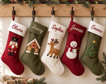 May include: Five hanging Christmas stockings in red, green, and white fabric. Each stocking features a personalised name embroidered on the cuff and a festive applique: a nutcracker, gingerbread house, reindeer, snowman, and Christmas tree.