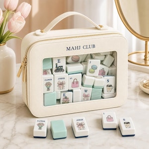 May include: A cream-colored rectangular carrying case with a clear front window, labeled MAHJ CLUB, containing various mahjong tiles. The tiles feature pastel illustrations of flowers, bows, handbags, and coffee cups. Five loose tiles sit in front.