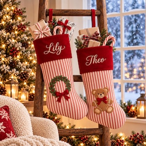 May include: Two personalised Christmas stockings hanging on a wooden ladder. The stockings feature red and white stripes, a red velvet cuff with the names Lily and Theo embroidered in white, a green wreath applique, and a brown teddy bear applique.
