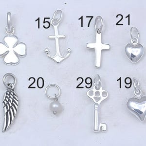 May include: A collection of ten silver charm pendants, including a four-leaf clover, anchor, cross, heart, angel wing, pearl, key, and two more hearts. The charms are numbered 6, 15, 17, 19, 20, 21, 28, and 29.