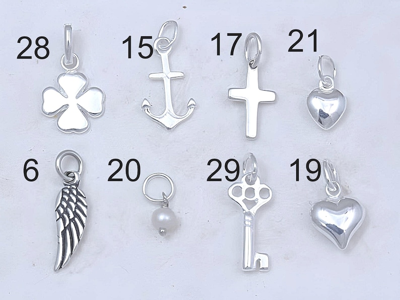 May include: A collection of ten silver charm pendants, including a four-leaf clover, anchor, cross, heart, angel wing, pearl, key, and two more hearts. The charms are numbered 6, 15, 17, 19, 20, 21, 28, and 29.