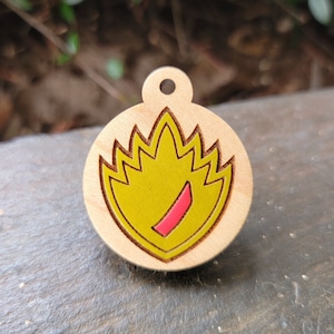 May include: A wooden keychain with a yellow and red flame design. The keychain is round and has a hole at the top for attaching to a key ring.