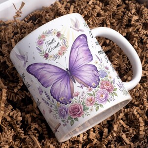 Può includere: Una tazza in ceramica bianca con una grande farfalla viola, una ghirlanda floreale con il testo Faith Wreath, colombe bianche in volo e grappoli di rose rosa e viola. Il design include testo aggiuntivo e rametti di lavanda sulla superficie.