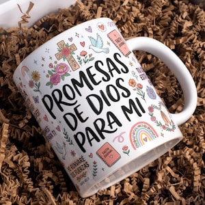 Op de afbeelding: Een witte keramische mok met de zwarte tekst Promesas de Dios para mi, omringd door kleurrijke illustraties van een kruis, bloemen, een duif, een regenboog en geloofsdagboeken. De tekst bevat Yo renvaré tus fuerzas en Isaías 40:31.