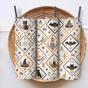 Può includere: Tre bicchieri cilindrici con cannucce nere, caratterizzati da un motivo a rombi ripetuto su sfondo bianco. Il design include illustrazioni di gatti neri, pipistrelli, cappelli da strega, ragnatele, fantasmi, boccette di pozioni e candele con fiori.