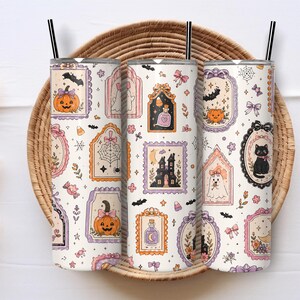 Può includere: Tre bicchieri cilindrici con cannucce nere caratterizzati da un motivo ripetuto di Halloween su sfondo color crema. Il design include zucche arancioni, gatti neri, fantasmi, case infestate, boccette di pozioni e caramelle in cornici ornate.