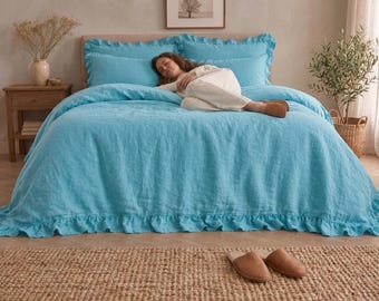 May include: A bright turquoise bedding set featuring a duvet cover and matching pillowcases with ruffled edges. The fabric has a visible linen-like texture. The set is draped over a bed, providing a solid color aesthetic for the bedroom space.