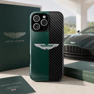 Op de afbeelding: Een smartphonehoesje met een gespleten ontwerp, bestaande uit een effen donkergroene kant en een zwarte kant met koolstofvezeltextuur. In het midden staat het zilveren en groene Aston Martin vleugellogo. De hoes heeft een uitsparing voor drie camera's.