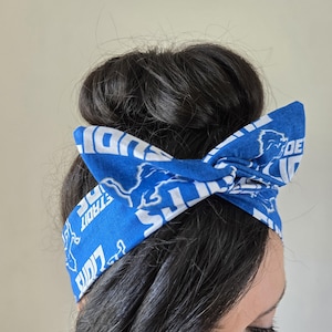 May include: Blue and white headband with the Detroit Lions logo and the words "Detroit Lions" repeated on the headband.