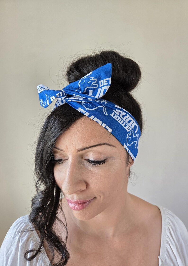 May include: A blue and white headband with the Detroit Lions logo and the text "Detroit Lions" repeated on the headband. The headband is tied in a bow on top of a person's head.