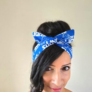 May include: A woman with long dark hair wearing a blue headband with white text and a lion logo. The headband is tied in a knot at the top of her head.