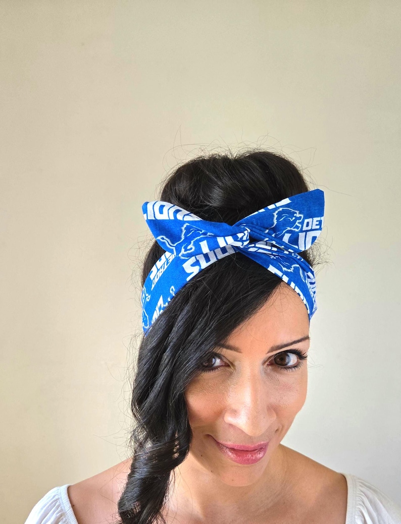 May include: A woman with long dark hair wearing a blue headband with white text and a lion logo. The headband is tied in a knot at the top of her head.