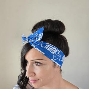 May include: A blue and white bandana headband with the text "DETROIT LIONS" and a lion graphic. The headband is tied around a woman's head.