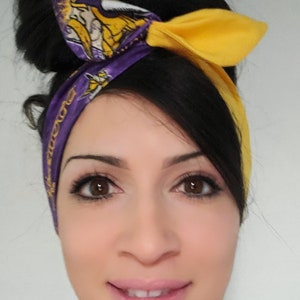 May include: A woman with dark hair is wearing a purple and yellow headband with a Minnesota Vikings logo. The headband is tied in a bow at the top of her head.