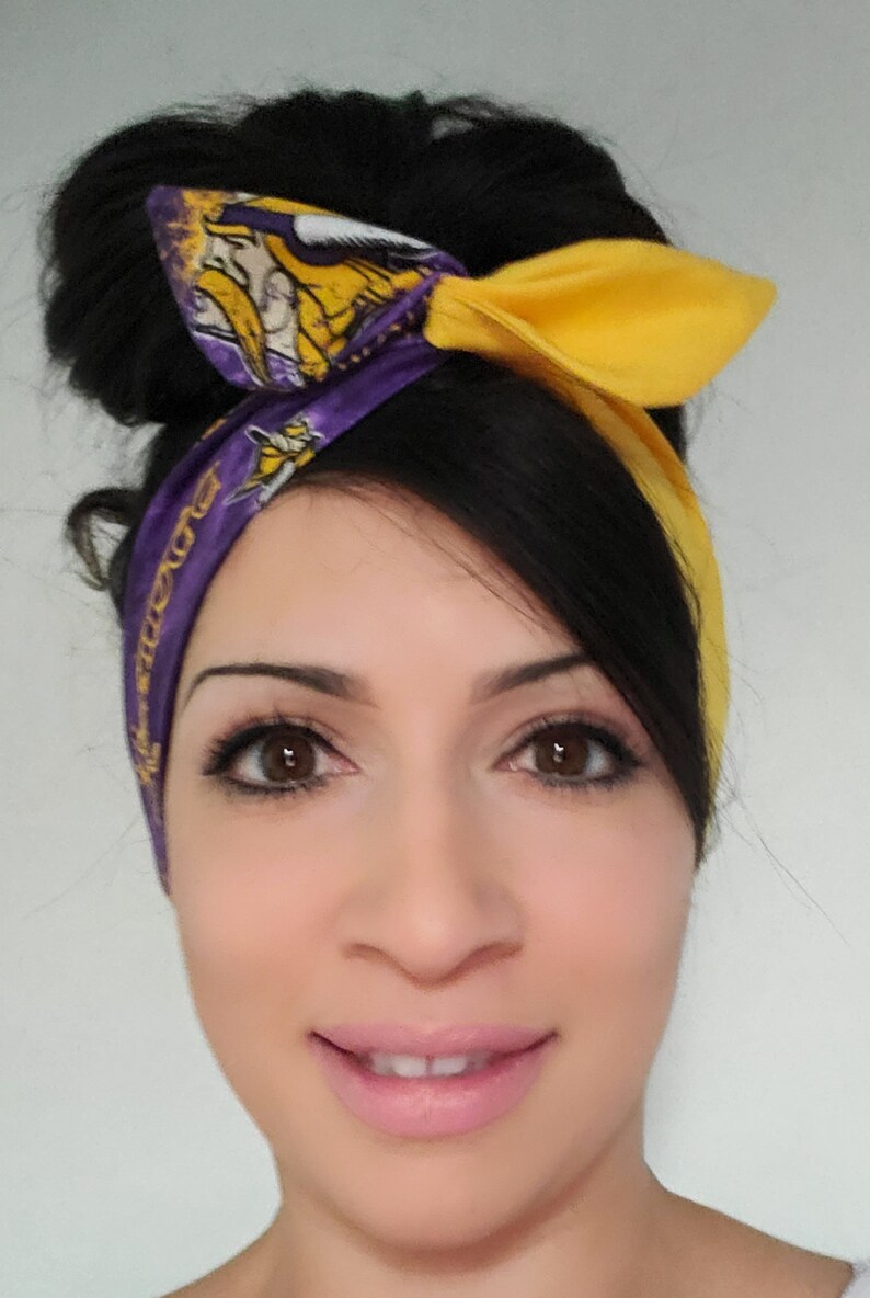 May include: A woman with dark hair is wearing a purple and yellow headband with a Minnesota Vikings logo. The headband is tied in a bow at the top of her head.