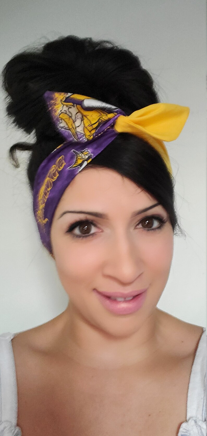 May include: A woman with dark hair wearing a purple and yellow headband with a team logo and the word "Vikings" on it. She is smiling and looking at the camera.
