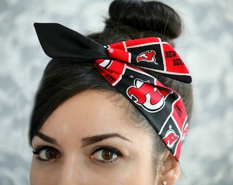 May include: A black and red headband featuring the New Jersey Devils logo and team name. The headband is tied in a bow on top of the head. The design includes the team logo and the words "NEW JERSEY DEVILS".