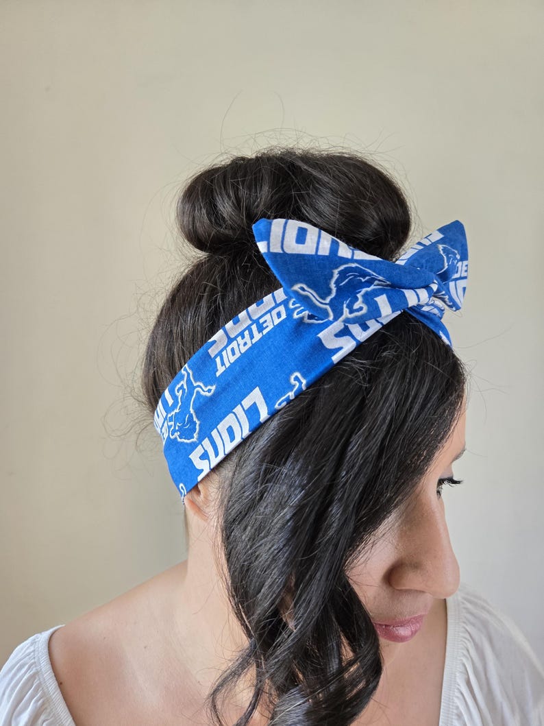 May include: A blue and white headband with the Detroit Lions logo and the words "Detroit Lions" repeated. The headband is tied in a bow on top of the head.