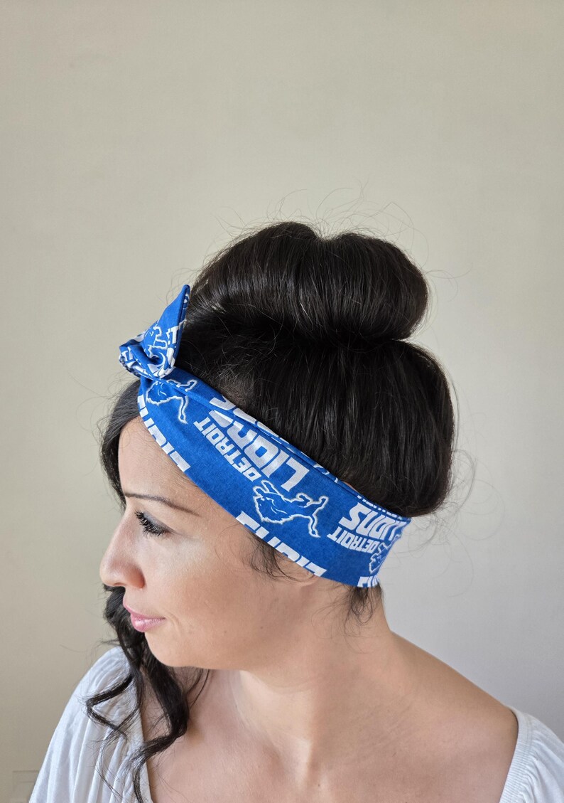 May include: A blue headband with a white print of the Detroit Lions logo and the words "Detroit Lions" repeated. The headband is tied in a knot on top of the head.