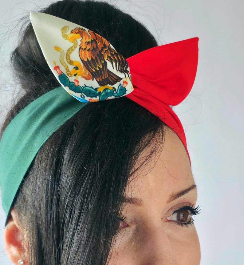 May include: A red, white, and green headband with a bow. The headband features the Mexican coat of arms on a white background. The design is a patriotic accessory, perfect for celebrating Mexican heritage or cultural events.