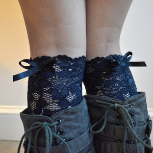 May include: A pair of black lace leg warmers with black satin bows. The leg warmers are worn with dark brown boots.