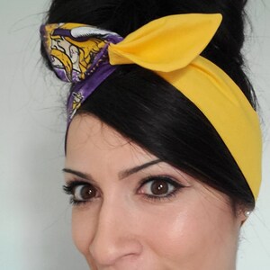 May include: A woman with dark hair styled in a bun wears a yellow headband with a purple and gold patterned section. The headband is tied in a bow at the top of her head.