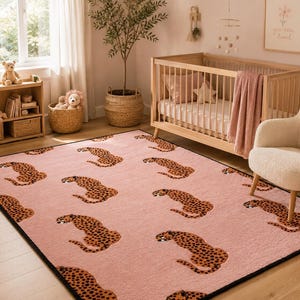 Könnte beinhalten: Ein rechteckiger Teppich mit einem sich wiederholenden Muster aus braunen und schwarzen Leopardenfiguren auf einem zartrosa Hintergrund. Der Teppich hat einen dunklen Rand und liegt auf einem hellen Holzboden in einem Raum mit Holzbett und cremefarbenem Sessel.