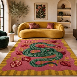May include: A rectangular area rug featuring a central pink field with a scalloped edge, decorated with a large green snake and multiple red pomegranate illustrations. The rug has a wide border with alternating yellow and gold vertical stripes.