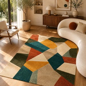 Könnte beinhalten: Ein rechteckiger Teppich mit einem geometrischen Muster aus kantigen Formen in Senfgelb, tiefem Petrol, Waldgrün, gebranntem Orange und Creme. Der Teppich hat einen strukturierten Flor und bedeckt einen Teil des hellen Holzbodens.