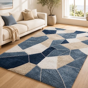Könnte beinhalten: Ein rechteckiger Teppich mit einem geometrischen Muster aus ineinandergreifenden Polygonen in Marineblau, Hellblau, Beige und Weiß. Der Teppich hat eine strukturierte, hochflorige Oberfläche mit klar definierten Linien zwischen den Farbblöcken.