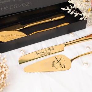 Può includere: Un set di posate dorate per servire torte composto da un coltello e una paletta, entrambi con incisioni personalizzate. Il coltello riporta i nomi Amelia & Make e la data 08.07.2026, mentre la paletta presenta un monogramma A&M.