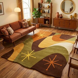 Op de afbeelding: Een groot vloerkleed met een abstract patroon van golvende, organische vormen in olijfgroen, mosterdgeel, bruin en crème. Het ontwerp bevat drie opvallende stervormige motieven in geel en oranje op een getextureerd oppervlak.