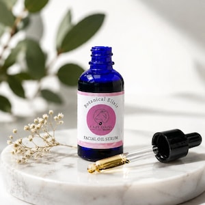 Puede incluir: Un frasco de vidrio azul cobalto de suero facial con un gotero negro. La etiqueta es rosa con un logotipo circular que muestra la silueta de una cabra y el texto Botanical Elixir, Lazy Daisy y Facial Oil Serum impreso en tinta negra.