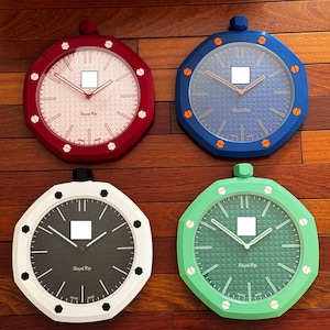 Op de afbeelding: Vier achthoekige wandklokken met getextureerde wijzerplaten en opvallende randen. De klokken zijn rood, blauw, wit en groen, elk voorzien van een kroon aan de bovenkant, uren- en minutenwijzers en de tekst Royal Pop en Swiss Made op de wijzerplaat.