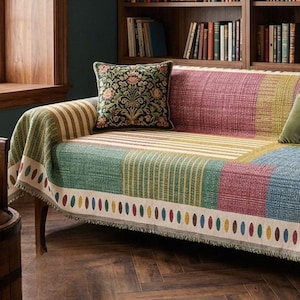 Può includere: Un copridivano tessuto multicolore caratterizzato da un design patchwork a righe e blocchi a tinta unita nelle tonalità del verde, rosso, giallo e blu, rifinito con un bordo color crema decorato da una fila di piccole forme ovali colorate.