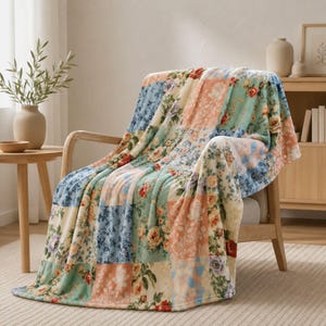 Può includere: Una morbida coperta con un design patchwork di vari motivi floreali nelle tonalità del blu, pesca, crema e verde. Il tessuto presenta diverse sezioni quadrate, ognuna con distinti motivi di rose e stampe botaniche, drappeggiata su una sedia in legno.