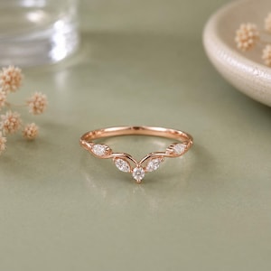 May include: A rose gold ring featuring a V-shaped band adorned with five small, clear, marquise-cut and round-cut stones arranged in a symmetrical pattern along the top, creating a delicate, pointed silhouette across the finger.